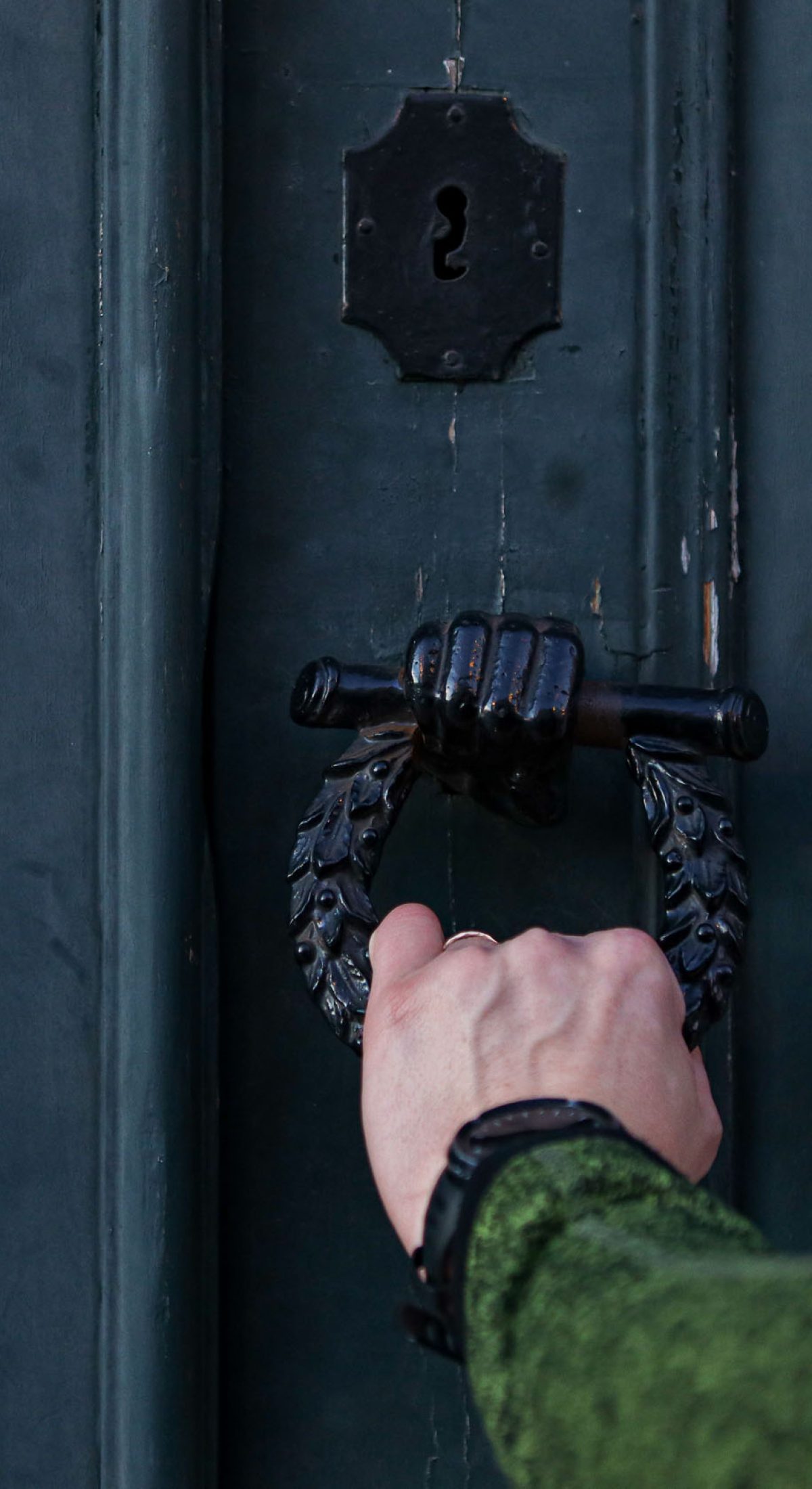 Man holds hand door handle or knocker of ancient wooden door.